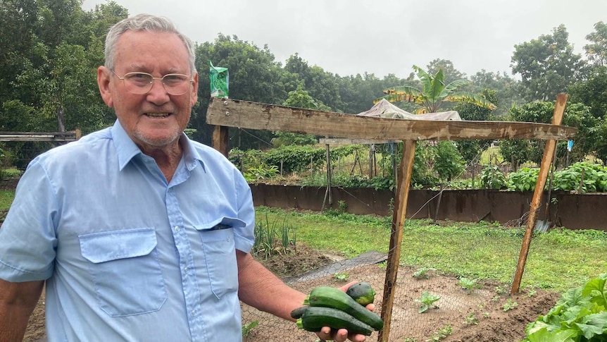 Old man standing in garden holding veggies