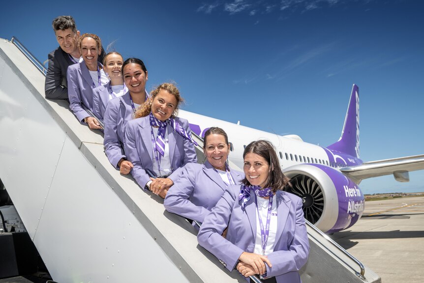 Bonza flight attendants on stairs of white plane, all smiling