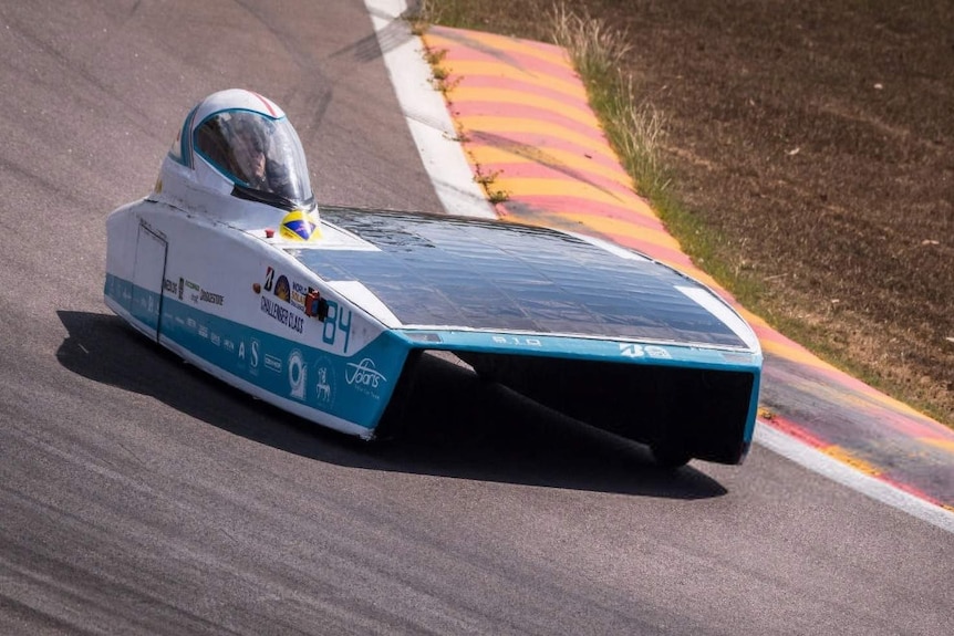 A sleek blue and white solar car handles a corner on a racetrack.