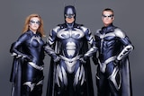 A Batman film promo poster featuring a woman and two men posing in chunky costumes, capes and masks