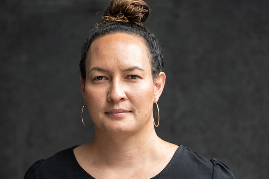 A woman with hoop earrings and her hair in a bun in front of a black backdrop