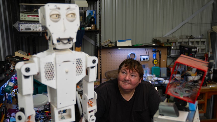 Robot artist Paul Aitken sits in his workshop looking up at a white robot called Fritz.