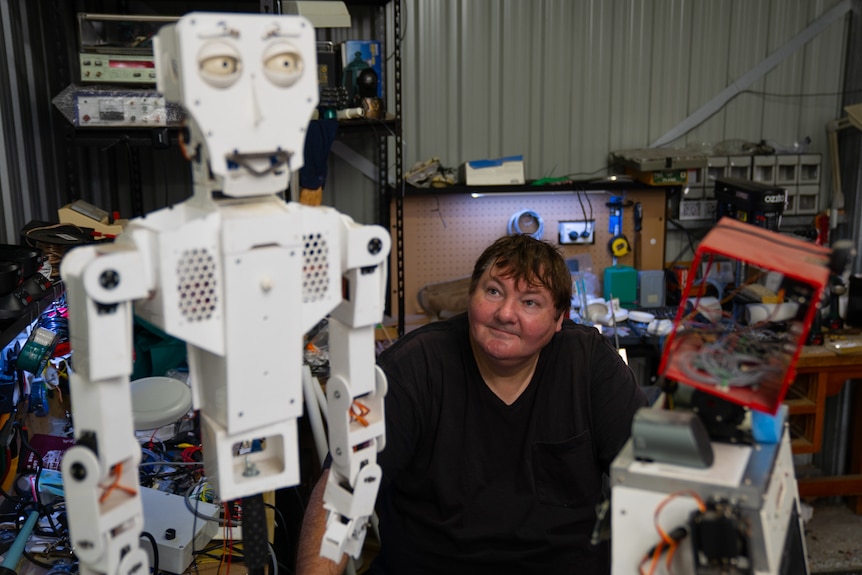 Robot artist Paul Aitken sits in his workshop looking up at a white robot called Fritz.