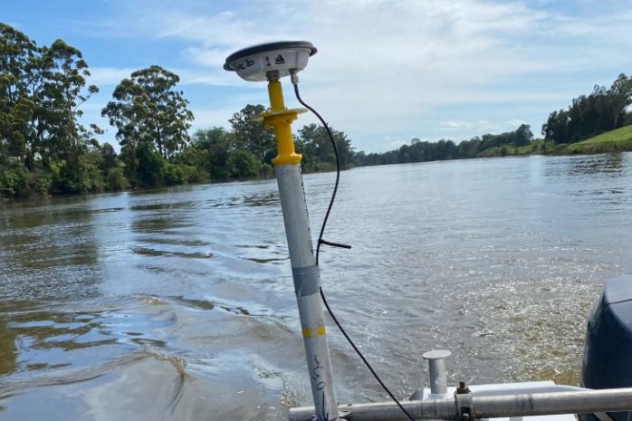 A device protrudes from the front on a boat with water visible in the background