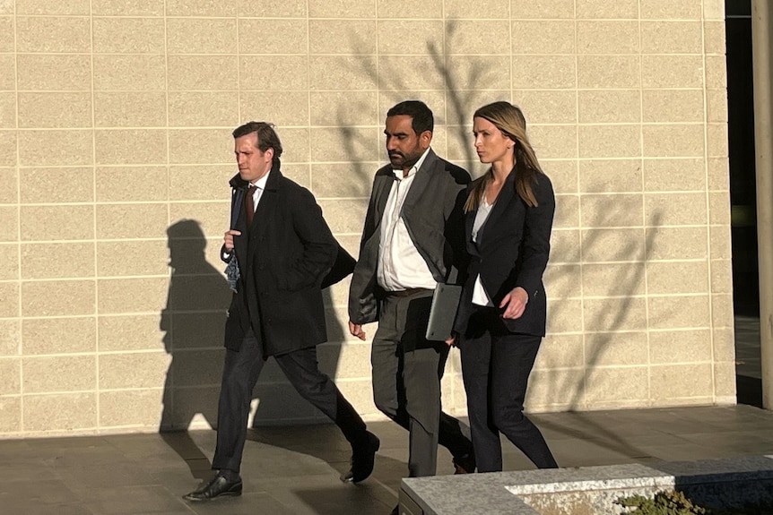 A man in a suit walks between two lawyers.