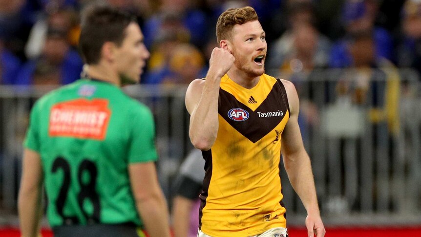A male AFL player pumps his right fist as he watches the ball go through the posts for a goal.