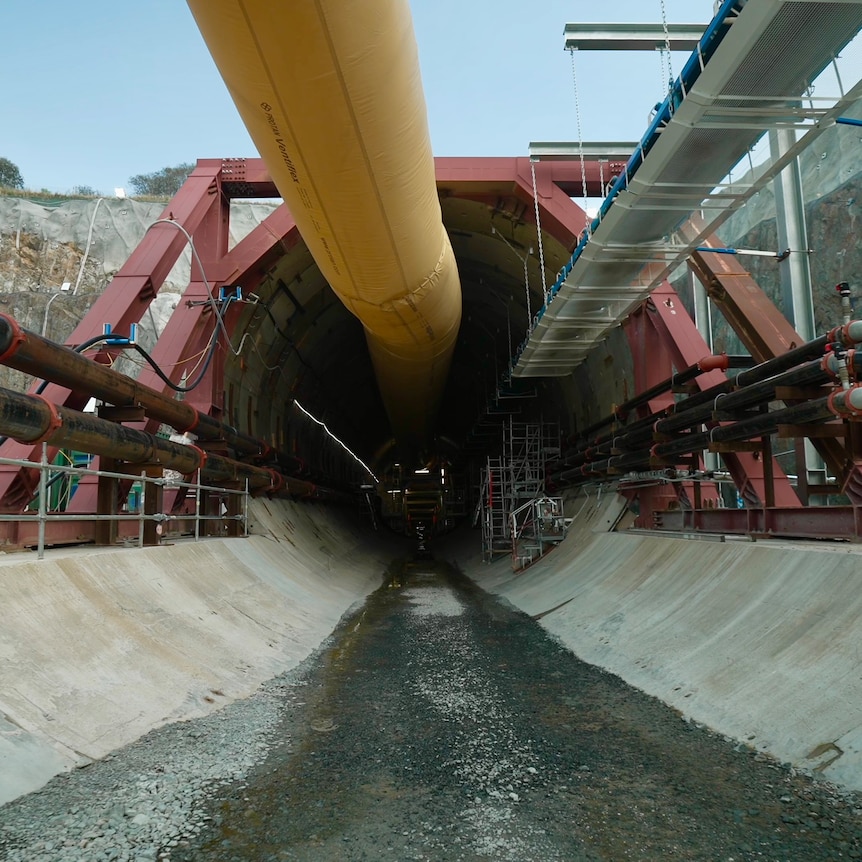 The entrance to a tunnel with a concrete floor, surrouned by industrial equipment.