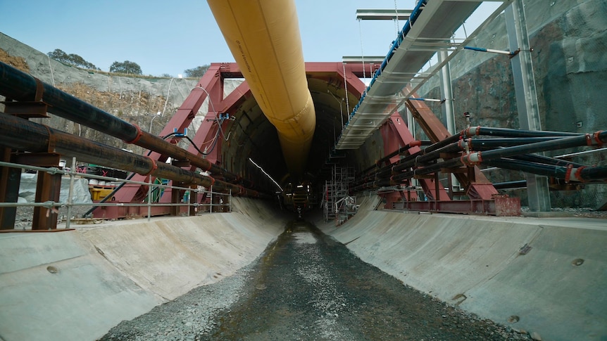 The entrance to a tunnel with a concrete floor, surrouned by industrial equipment. 