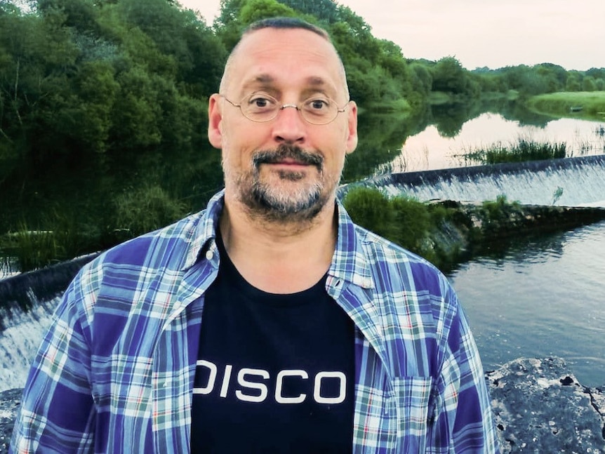 Morgan stands in nature, wearing glasses and a shirt that says 'disco.'