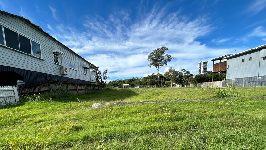 An image of green grass, blue sky with white clouds, and two houses bordering the grass on the left and right.