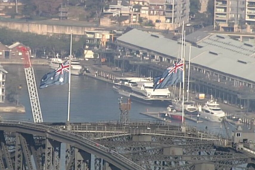 two australian flags above a bridge at half-mast