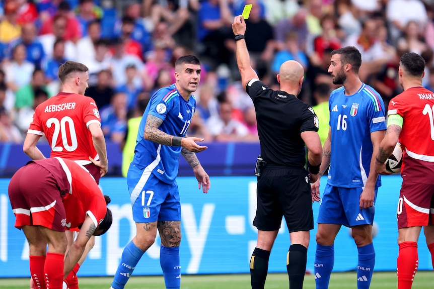 An Italy player is shown a yellow card by the referee against Denmark at Euro 2024.