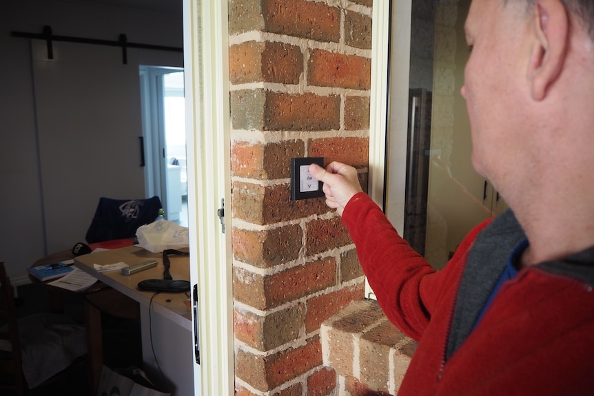 A man presses a button on a brick wall outside a house.