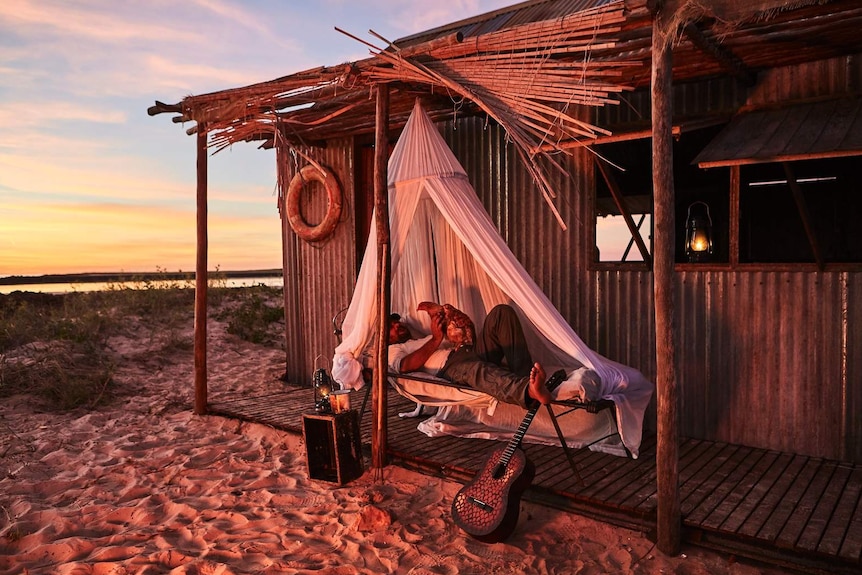 Warwick Thornton lies on a bed outside his shack holding a chicken in The Beach documentary.