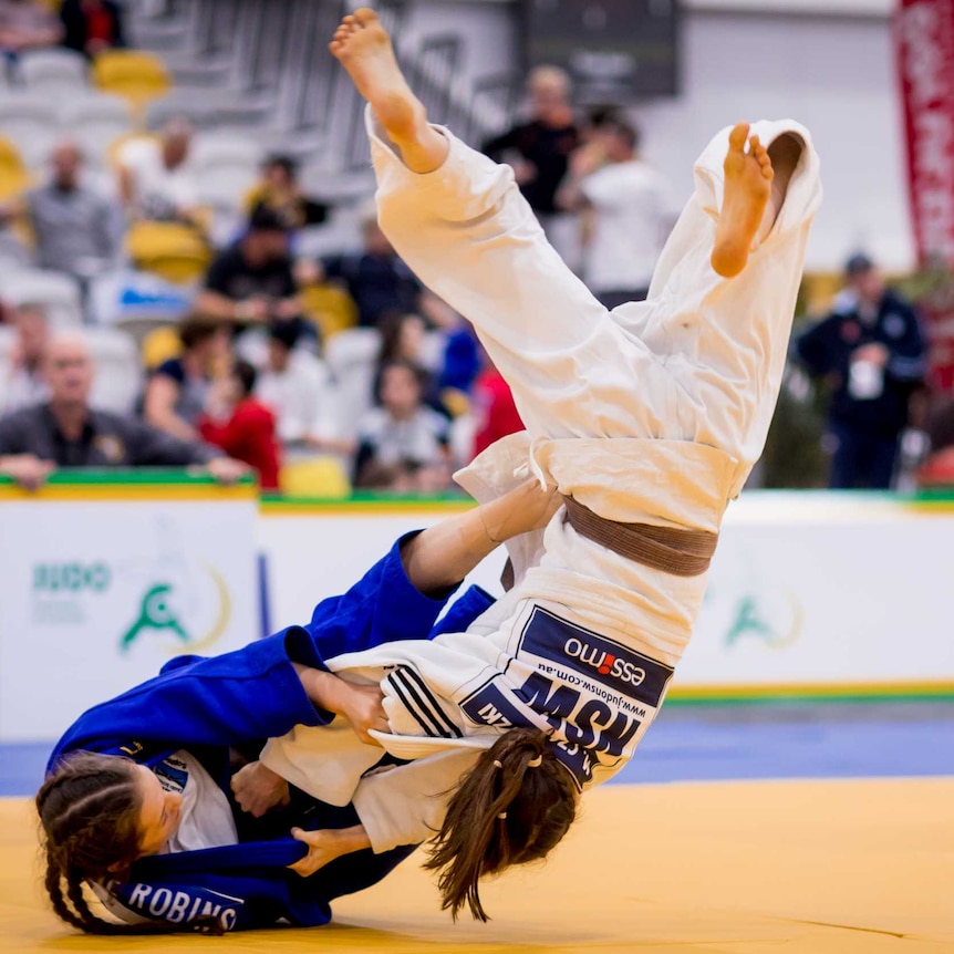 Sophie Robins throws a brown-belt competitor. She is on the ground and uses her leg to push the girl into the air.