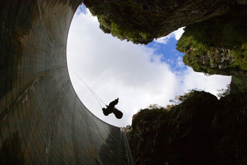 Looking up at person abseiling at a dam wall.