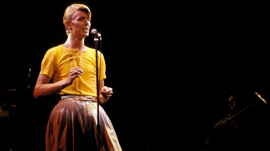 David Bowie performs onstage in a yellow shirt and large pants