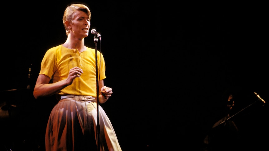 David Bowie performs onstage in a yellow shirt and large pants