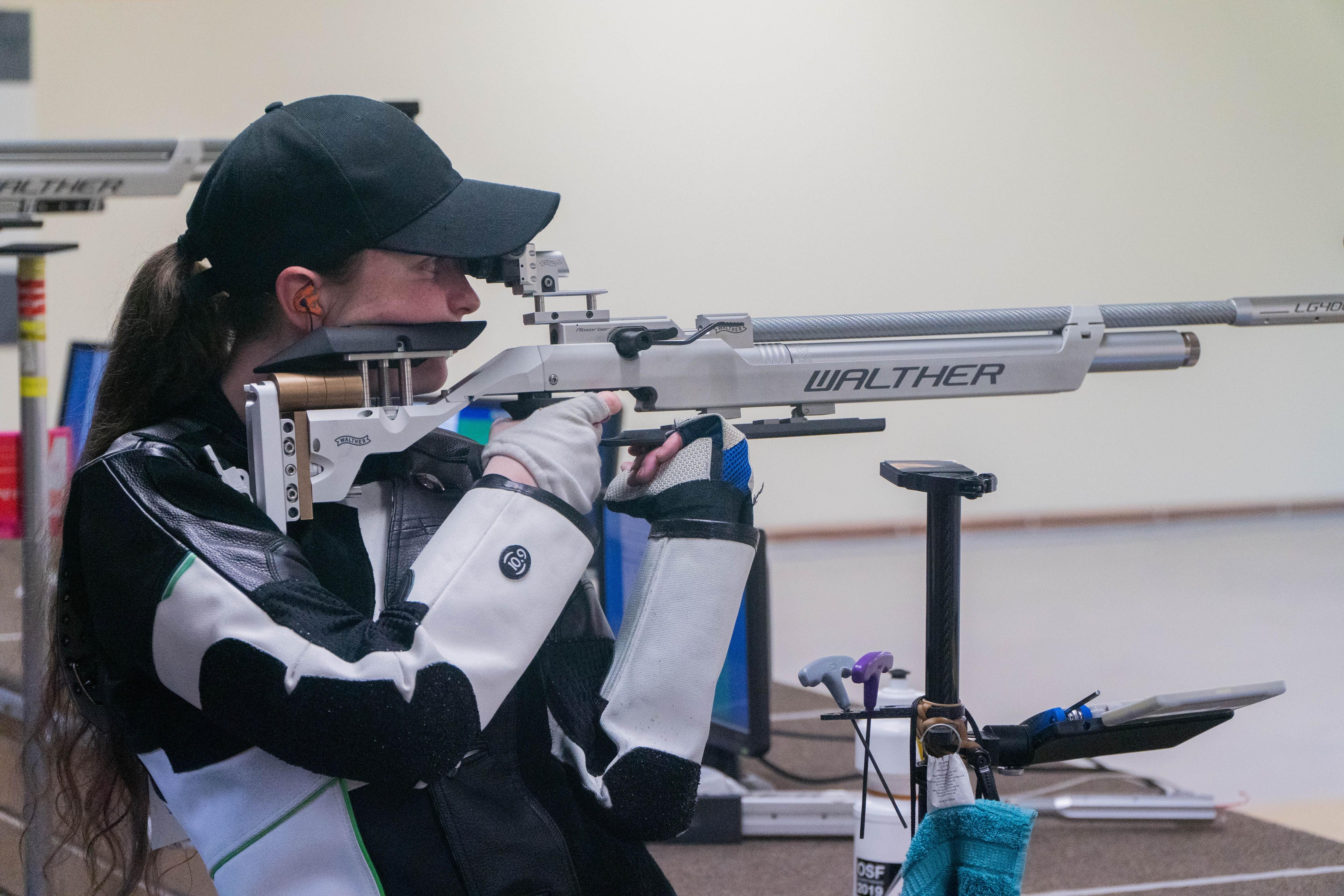 Elise Collier holds a rifle on her shoulder and aims down the sights