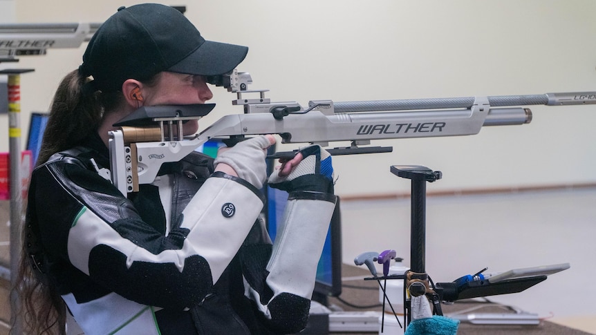 Elise Collier holds a rifle on her shoulder and aims down the sights
