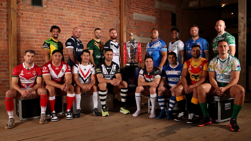 Men's rugby league captains pose with the World Cup trophy in front of exposed brick walls.