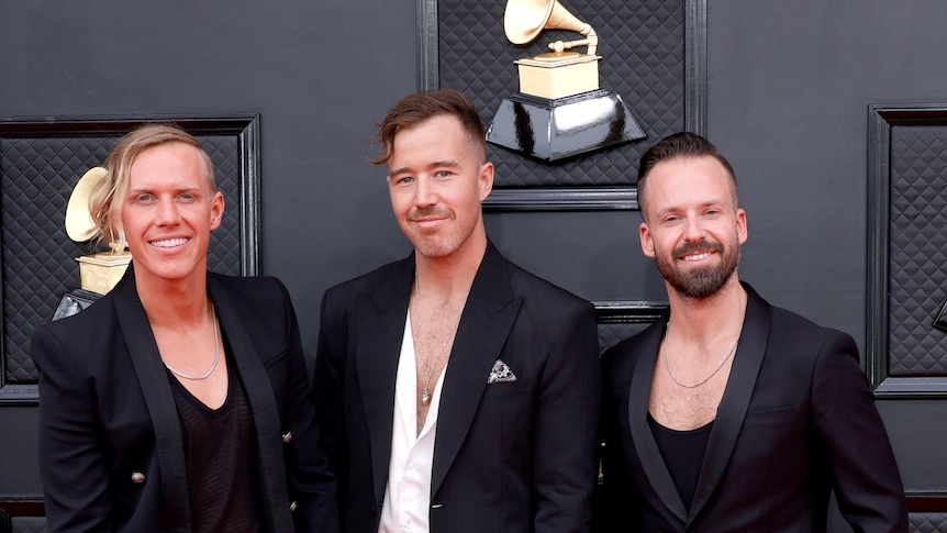 RÜFÜS DU SOL dressed in formal attire and smiling on the red carpet of the 2022 Grammy Awards red carpet