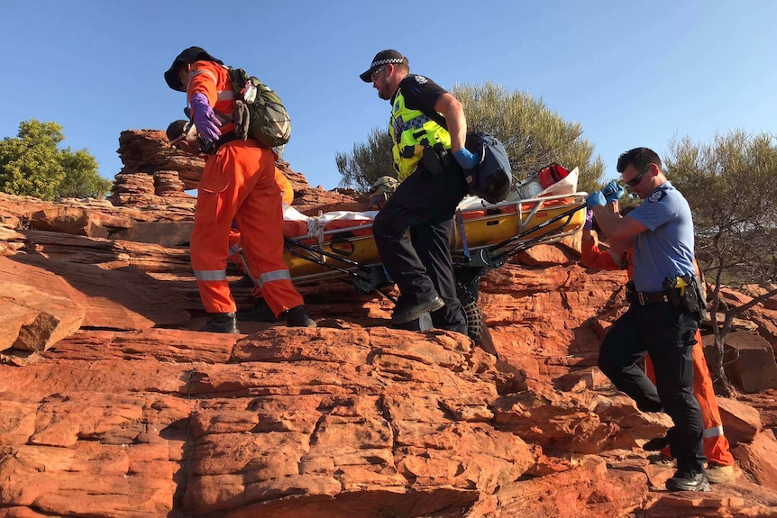 Six people in police and SES uniforms carry a stretcher up the side of a red rockface