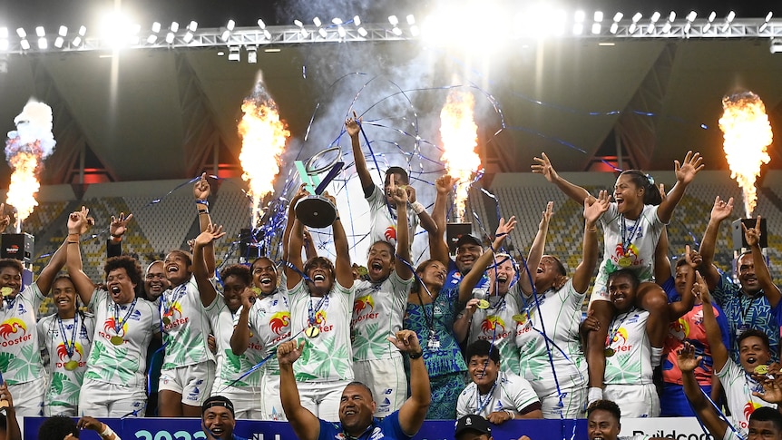 Fijiana Drua celebrate with the Super W trophy as fireworks go off behind them