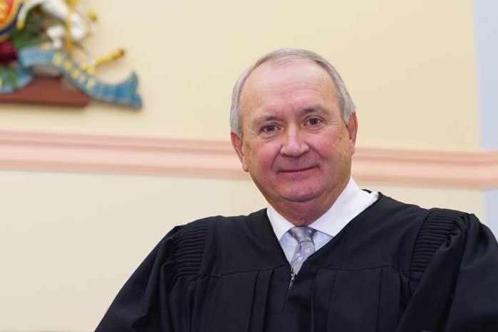 A judge stands in front of the bench in a courtroom.