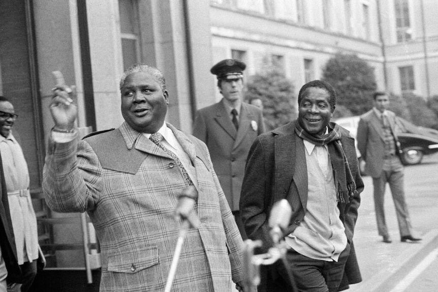 A black and white photo shows Joshua Nkomo and Robert Mugabe walking out the front door of an old European building.