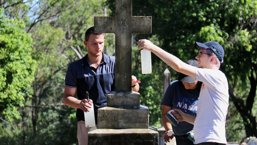 Three people clean a headstone in South Brisbane Cemetary.