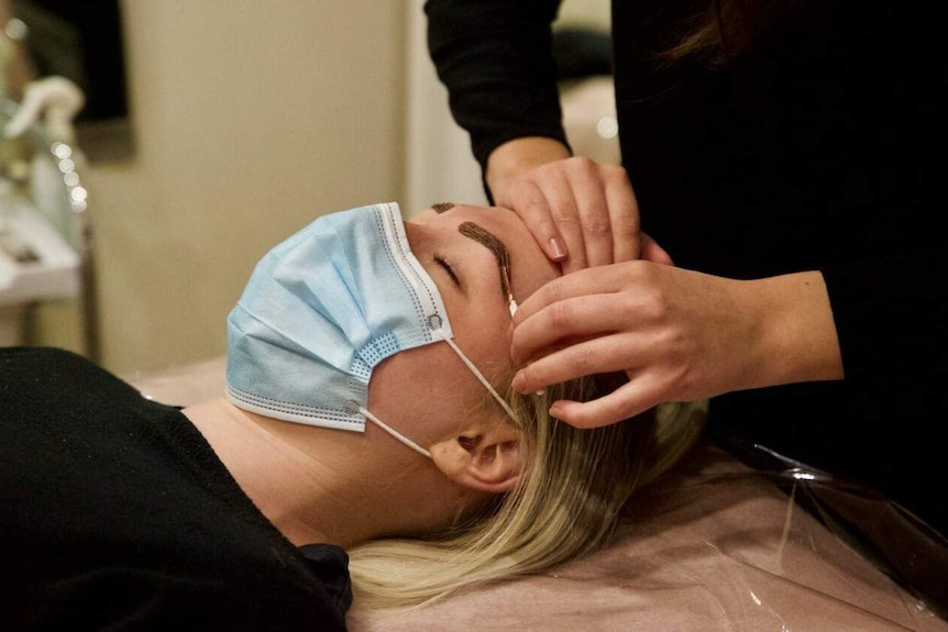 A close up of a beautician waxing a women's eyebrow.
