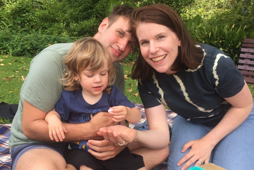 Lyndal Malarkey sitting with her husband and son in front of a birthday cake in a park