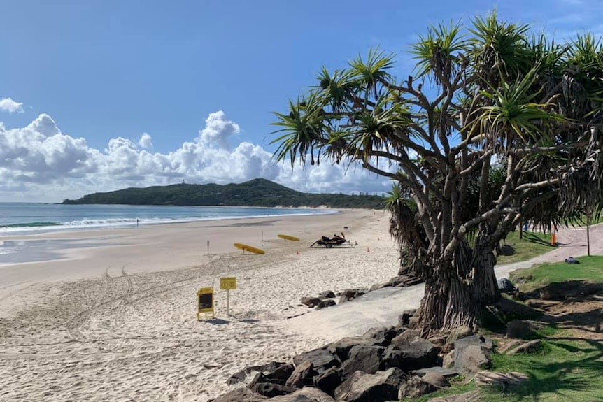 An empty beach stretches into the distance on a sunny day in Byron Bay