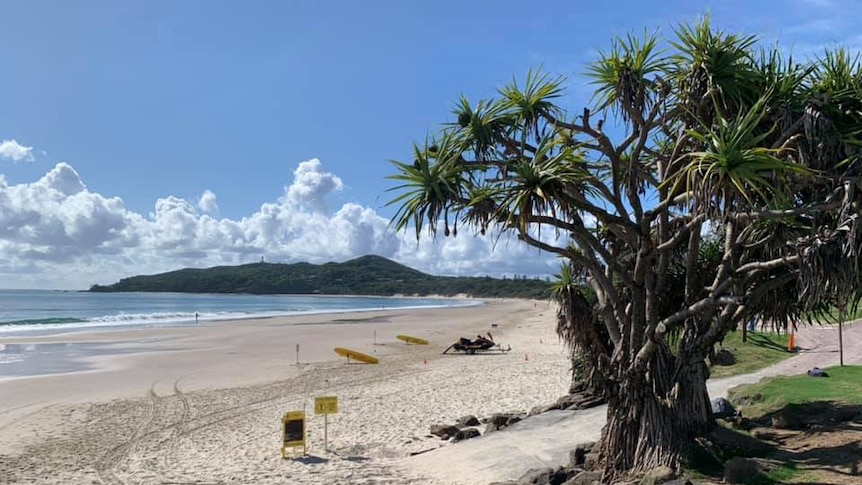 An empty beach stretches into the distance on a sunny day in Byron Bay