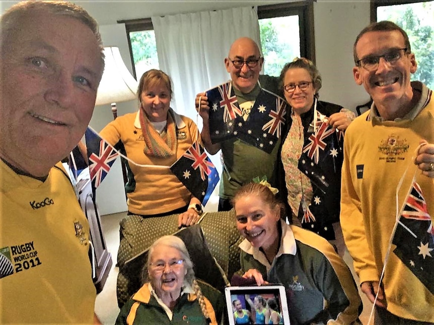 A group of seven people in Australian jerseys and holding Australian flags.  One woman holds a photo of her daughter.