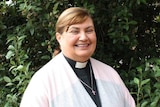 A smiling woman wearing a clerical collar and cross around her neck.