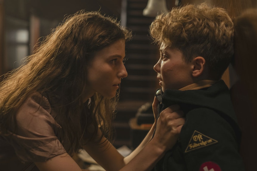 A girl holding a younger boy up against a wall by his coat collar