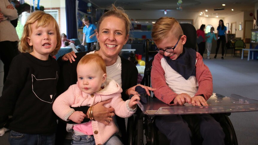 A young boy in a wheelchair, with a smiling woman and two young children.