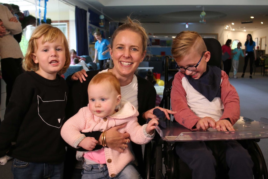 A young boy in a wheelchair, with a smiling woman and two young children.