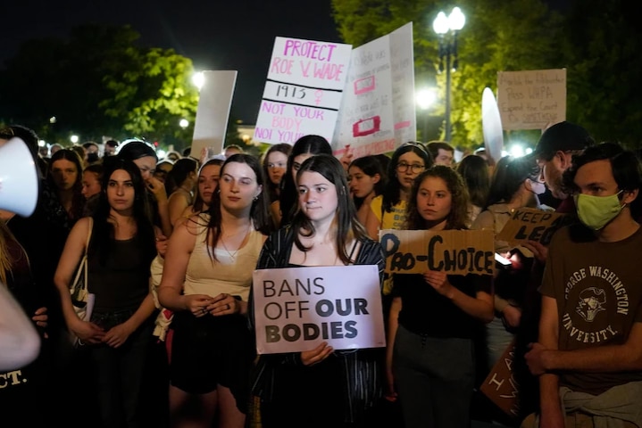 A group of women stands in the dark, holding banners which writes "BANS OFF OUR BODIES".