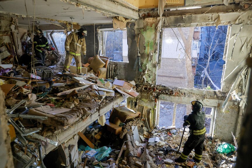 Two men stand inside an apartment that has been destroyed by shelling with debris and destruction everywhere. 