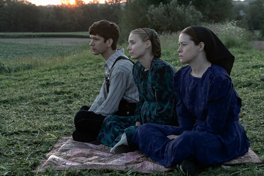 Two women and a man sit in a blanket on the grass