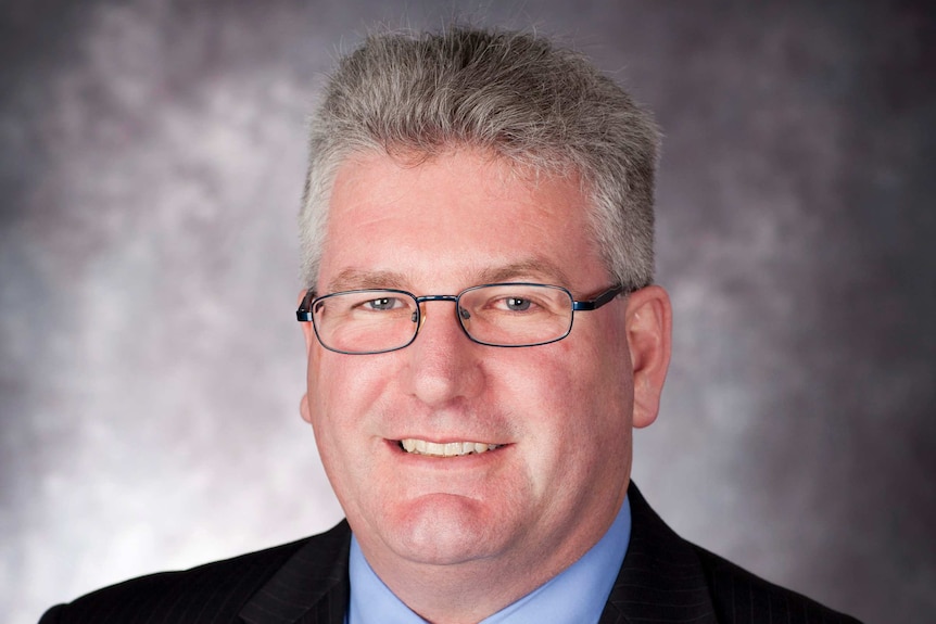 A portrait of David Morton, he is in a suit and tie with grey hair and glasses.