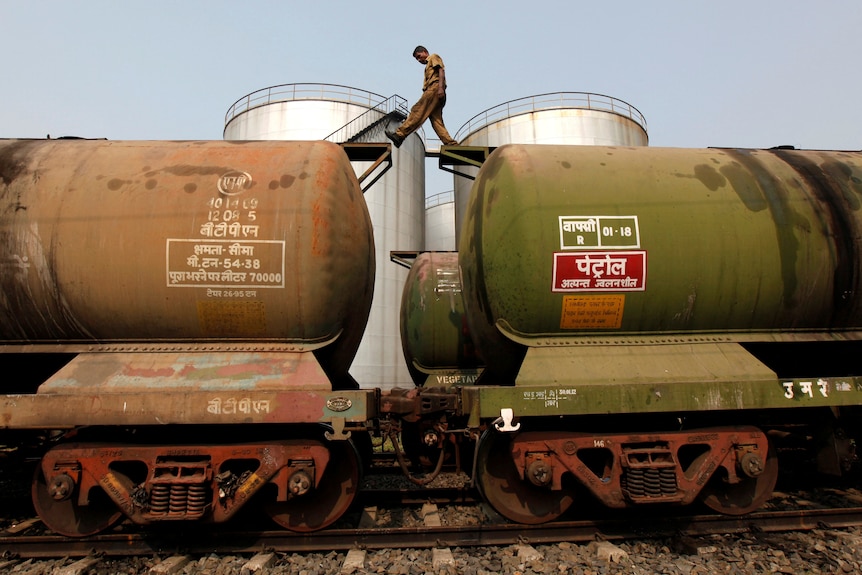A worker walks between two cylindrical metal train tanker cars.