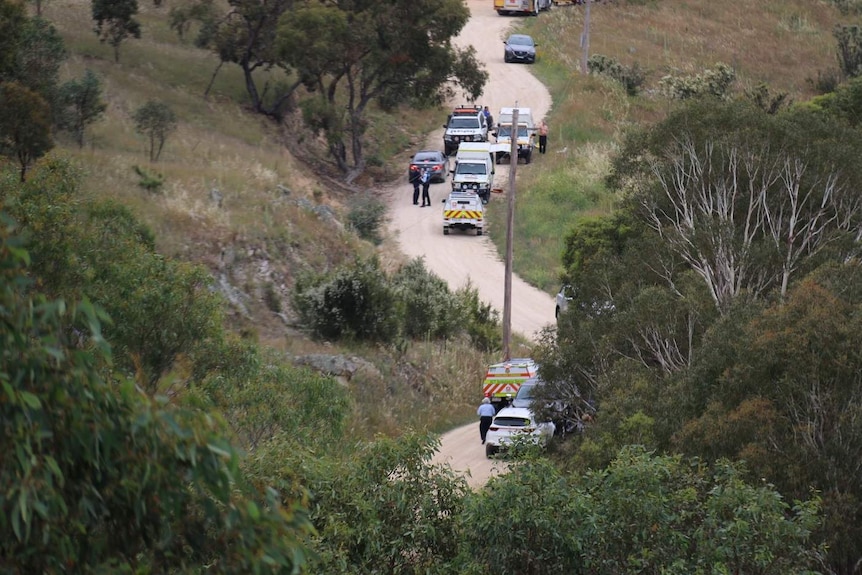 Several emergency services vehicles on a dirt road. One man is loitering shirtless.