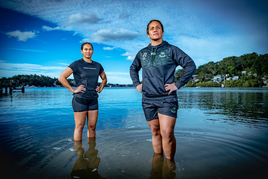 Two women stand in the water, hands on their hips, looking beyond the camera with contemplative looks.