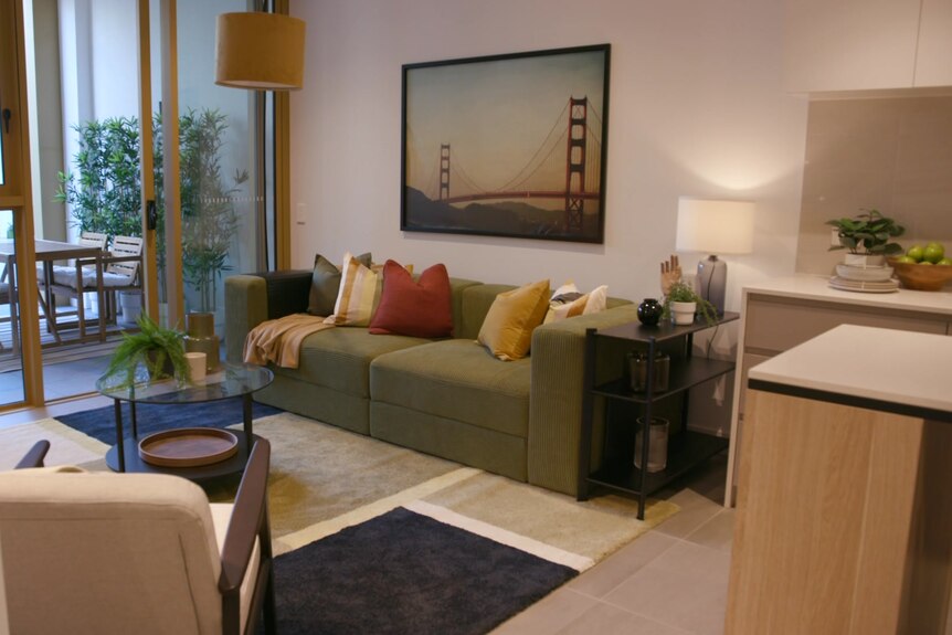 A green sofa against the wall with red and yellow cushions and a picture of a bridge on the wall