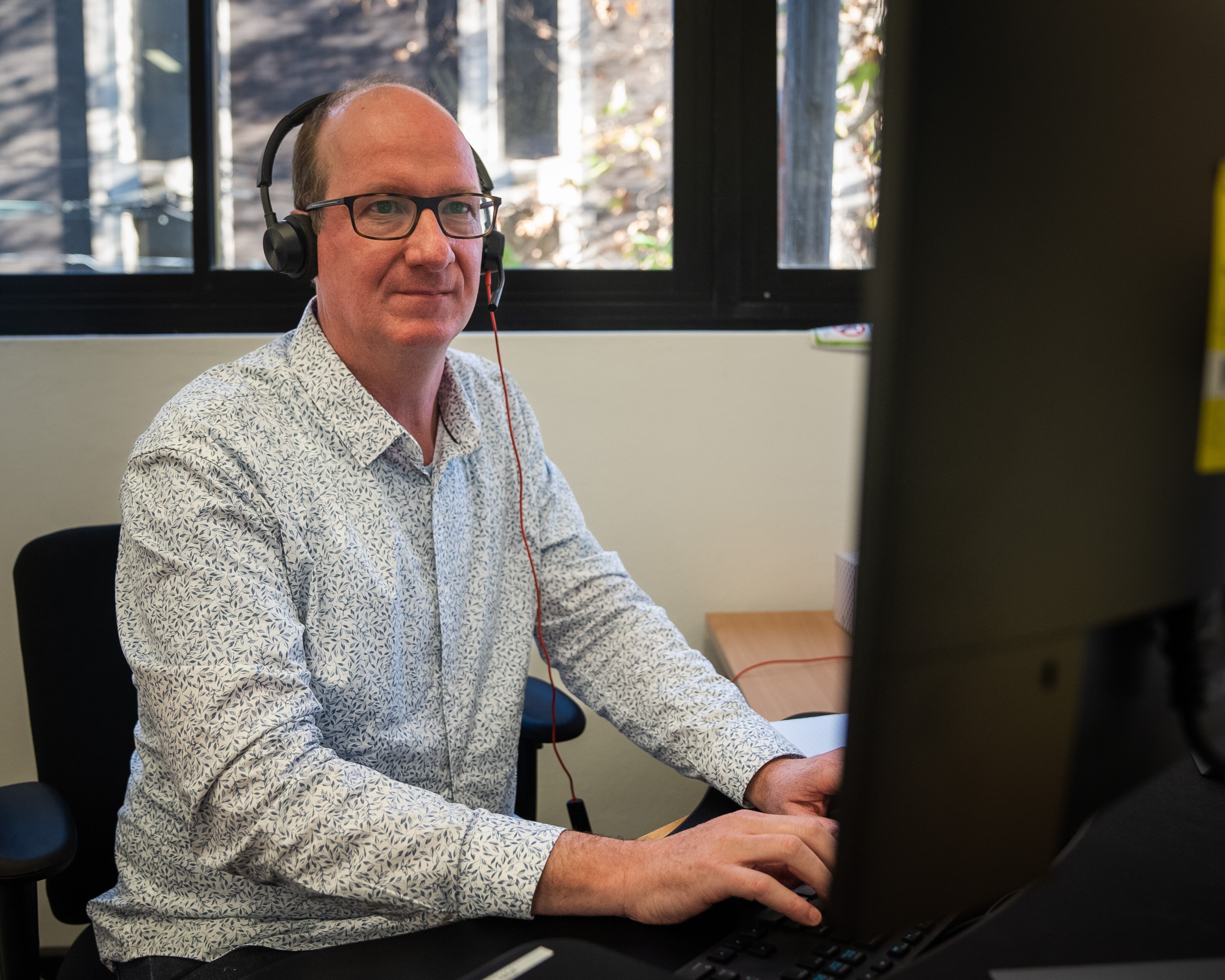 Peter Thompson works at desktop computer wearing headset.