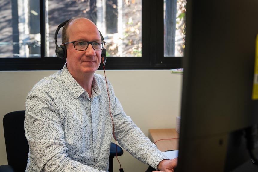 Peter Thompson works at desktop computer wearing headset.